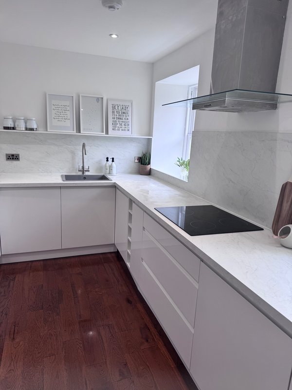 Modern white kitchen with marble countertops, induction hob, and wooden floor