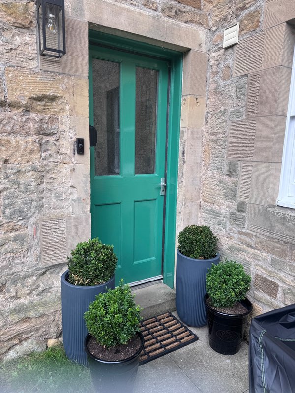 Stone cottage entrance with bright green door, potted plants, and dark mat