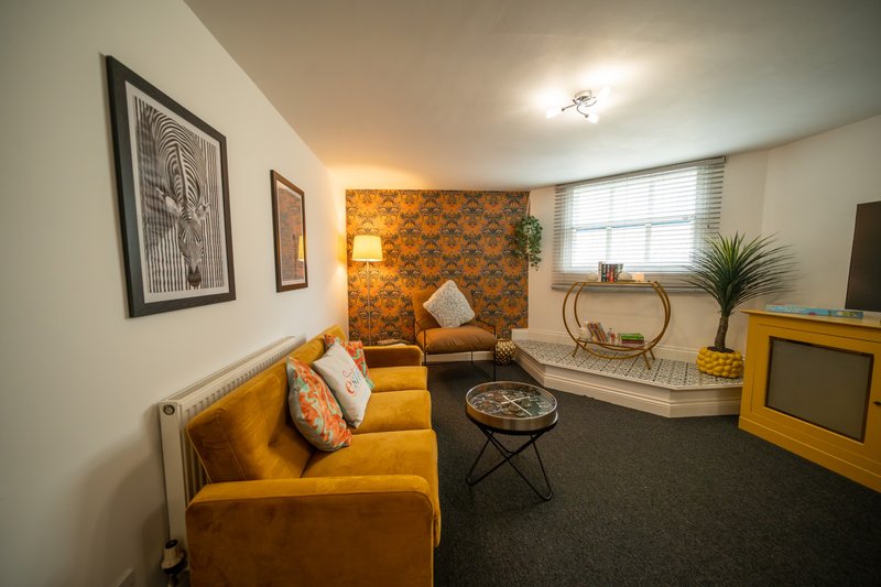 Stylish living room with mustard velvet sofa, patterned accent wall, framed artwork and television