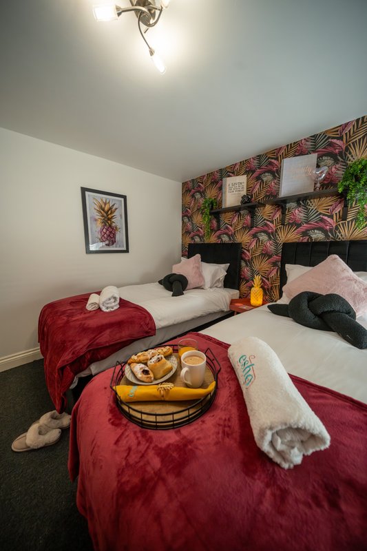 Bedroom with twin beds, colorful tropical wallpaper, red bedding, and welcome refreshments