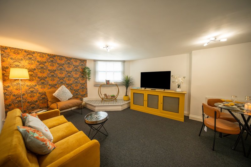 Modern living room with yellow sofa, patterned accent wall, TV unit, and dining area