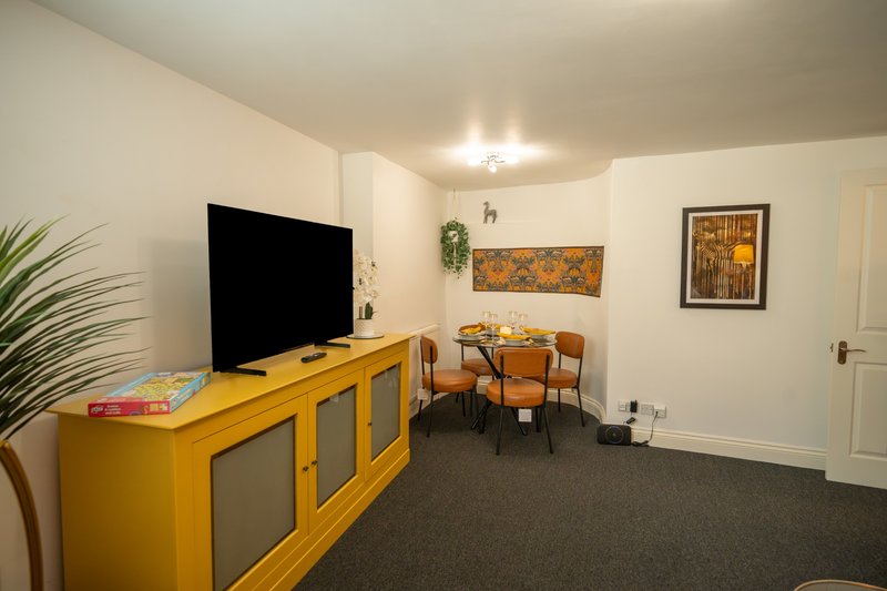 Living room with yellow TV stand, flat-screen TV, dining table with chairs, and potted plant