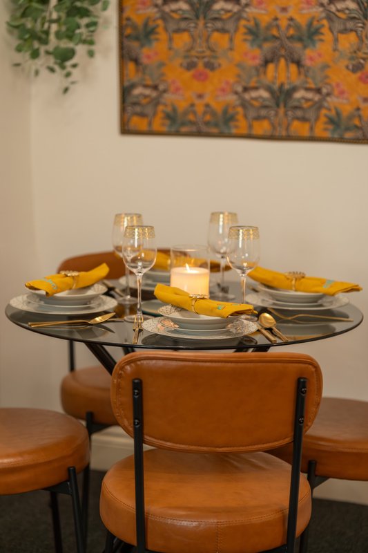 Dining table set with place settings, glasses, yellow napkins and leather chairs