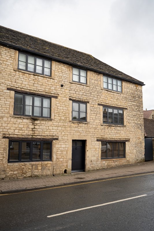 Stone-built three-story residential house with dark-framed windows and black door
