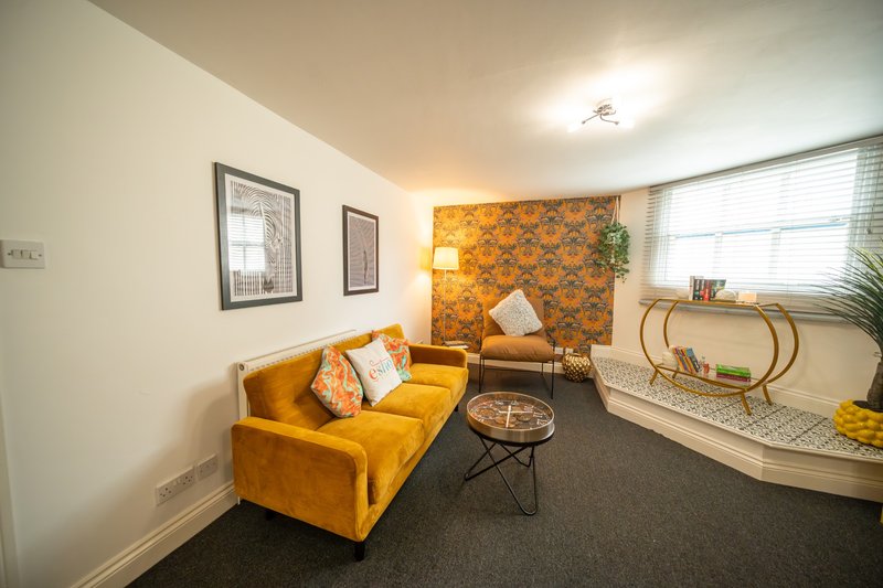 Modern living room with yellow sofa, patterned accent wall, coffee table and window seating area