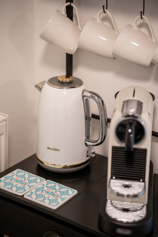 Kitchen counter with white electric kettle, coffee machine, and hanging mugs