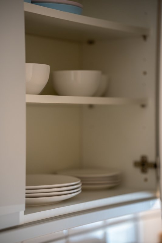 Open kitchen cabinet with white dishes, bowls and stacked plates on shelves