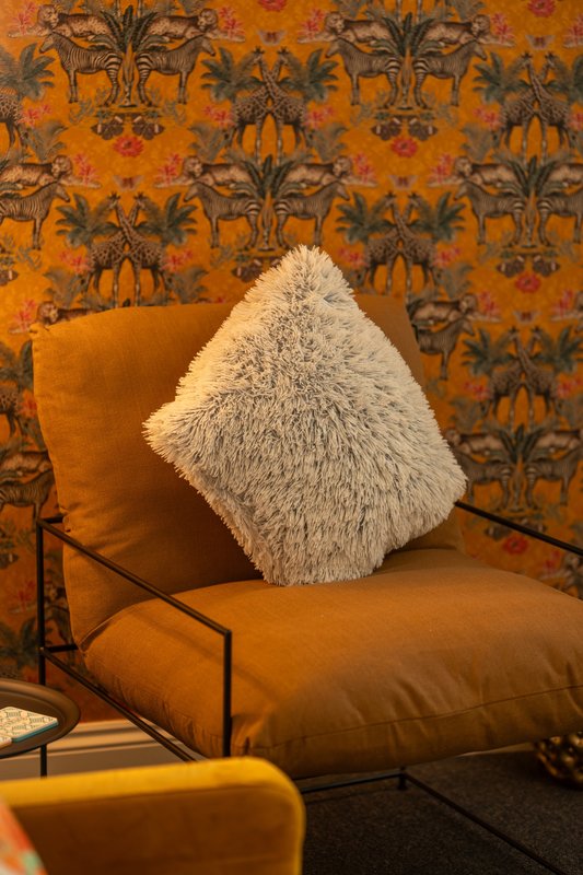 Orange upholstered chair with fluffy white cushion against patterned wallpaper