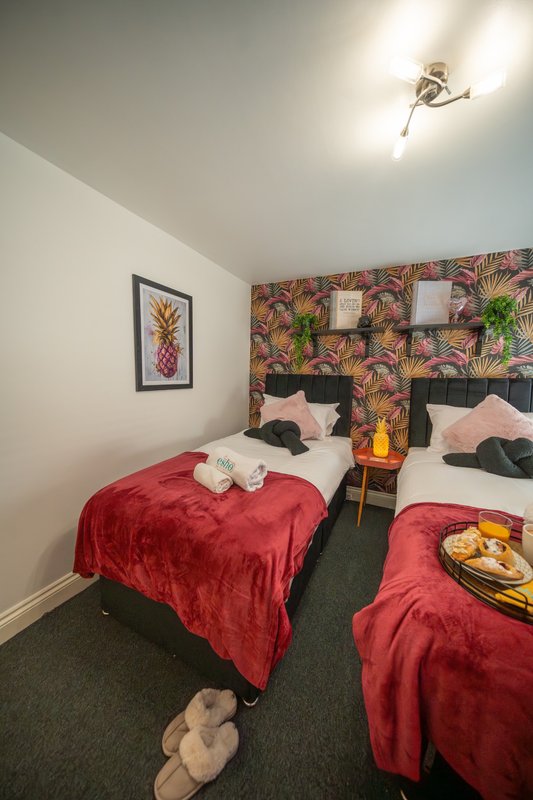 Twin bedroom with red velvet bedspreads, tropical patterned headboard and framed pineapple artwork