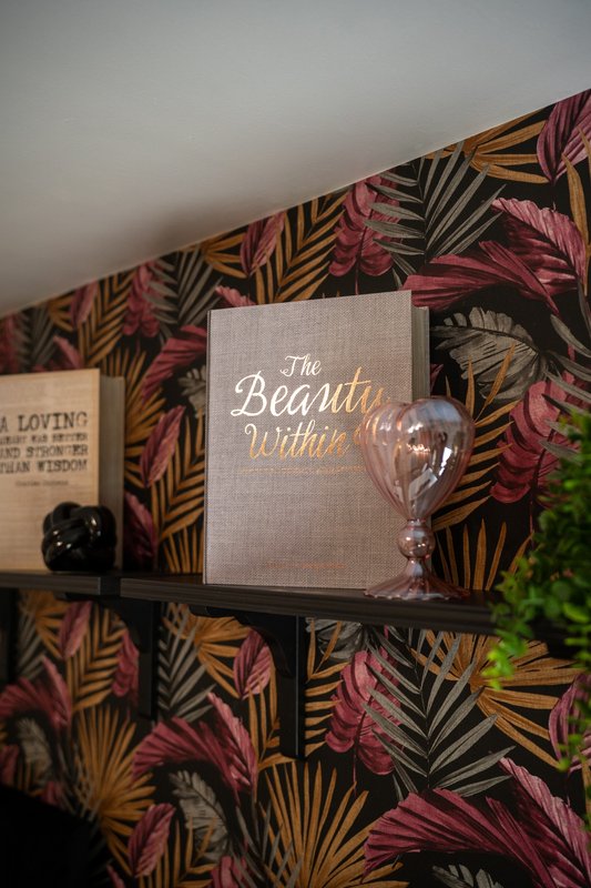 Shelf with decorative book, black candle, and potted plant against patterned wallpaper