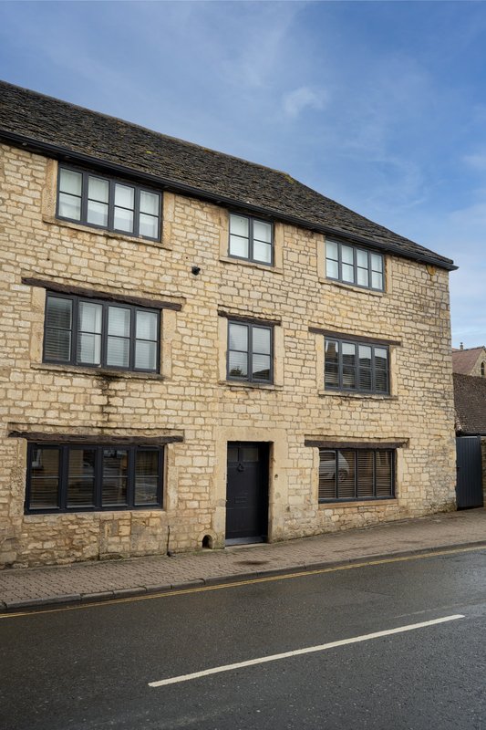 Three-storey stone building with multiple windows and dark door on street frontage