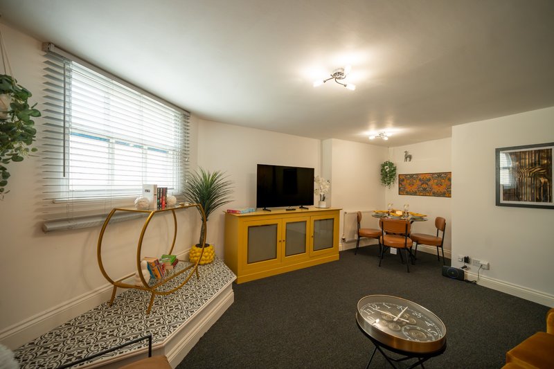 Bright living room with yellow TV unit, seating area, window with blinds and potted plants