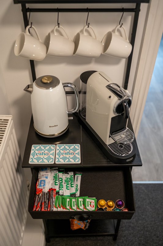 Coffee station with mugs, kettle, espresso machine and supplies shelf