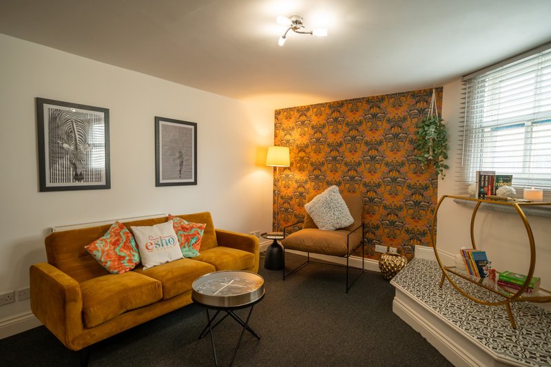 Living room with orange velvet sofa, patterned accent wall, framed artwork, and large windows