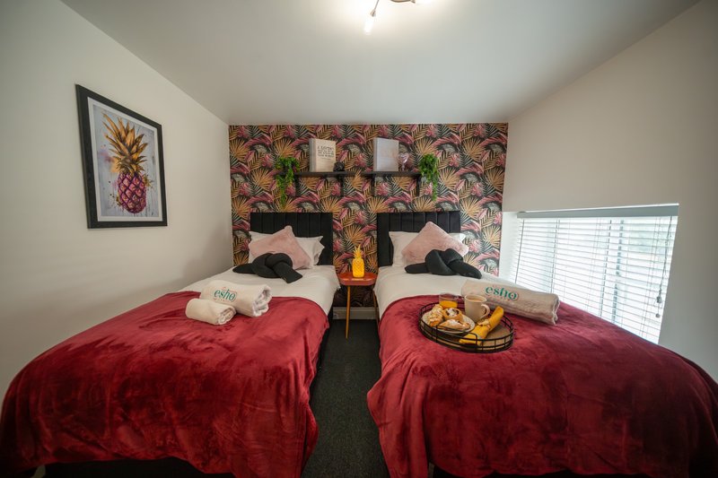 Twin bedroom with red bedding, patterned headboard, framed pineapple art and potted plants