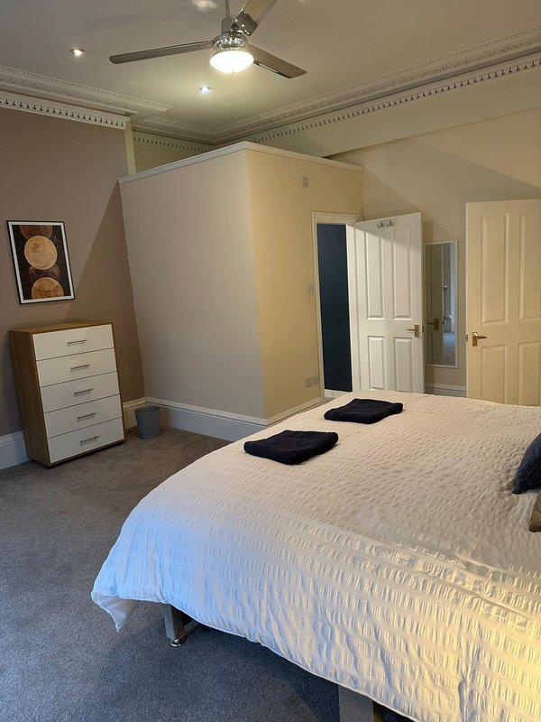 Spacious bedroom with double bed, white dresser, ceiling fan, and multiple doors