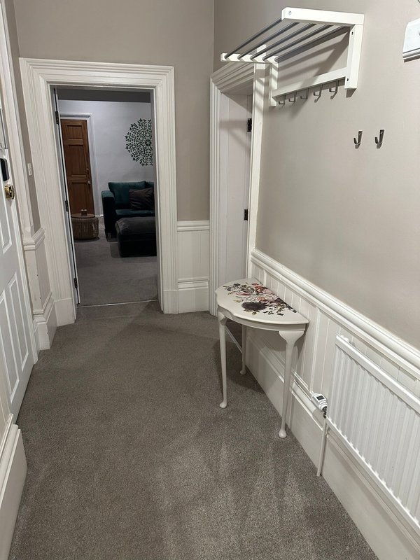 Hallway with white trim, grey carpet, small table and coat rack leading to living room