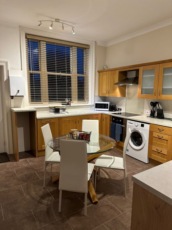 Kitchen-diner with wooden cabinets, dining table, washing machine and window with shutters