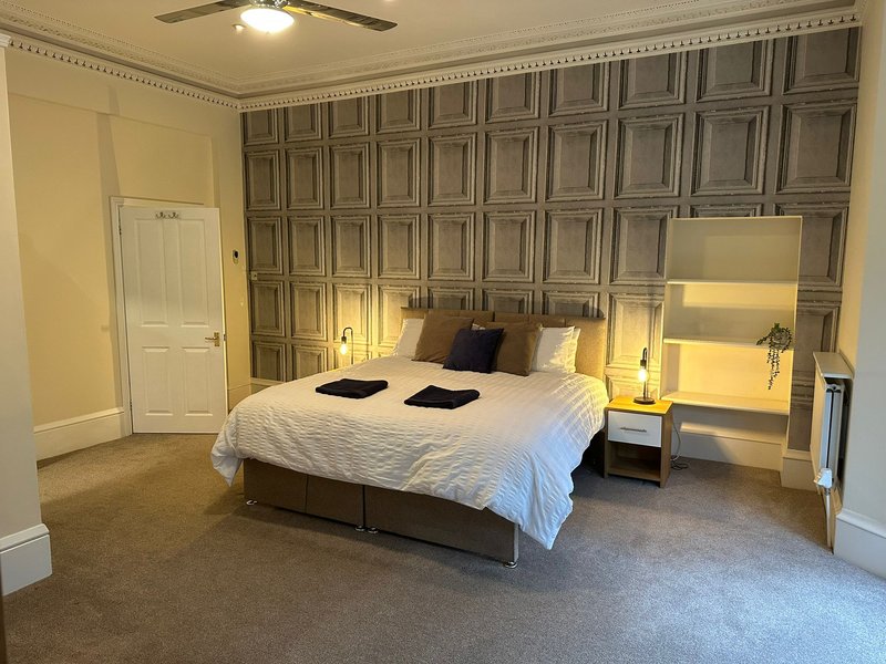 Spacious bedroom with king bed, panelled feature wall, bedside lamps, and wooden door