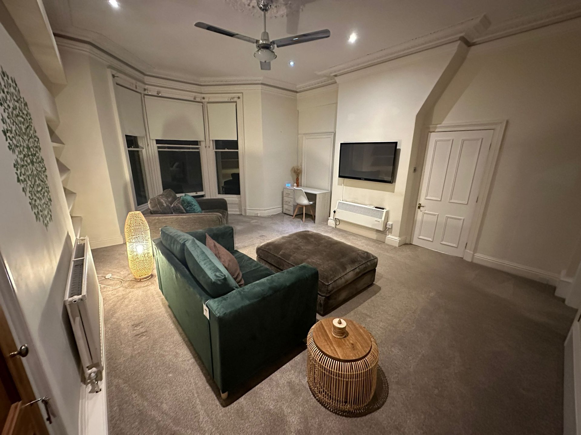 Spacious living room with green sofa, TV, ceiling fan, and large windows