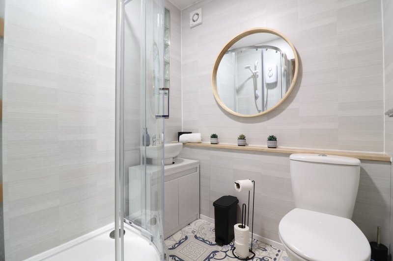 Modern bathroom with shower cubicle, vanity sink, round mirror and toilet