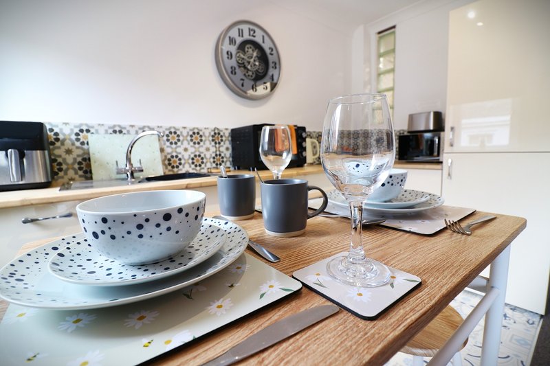 Modern kitchen with wooden island, place settings, wine glasses and wall clock