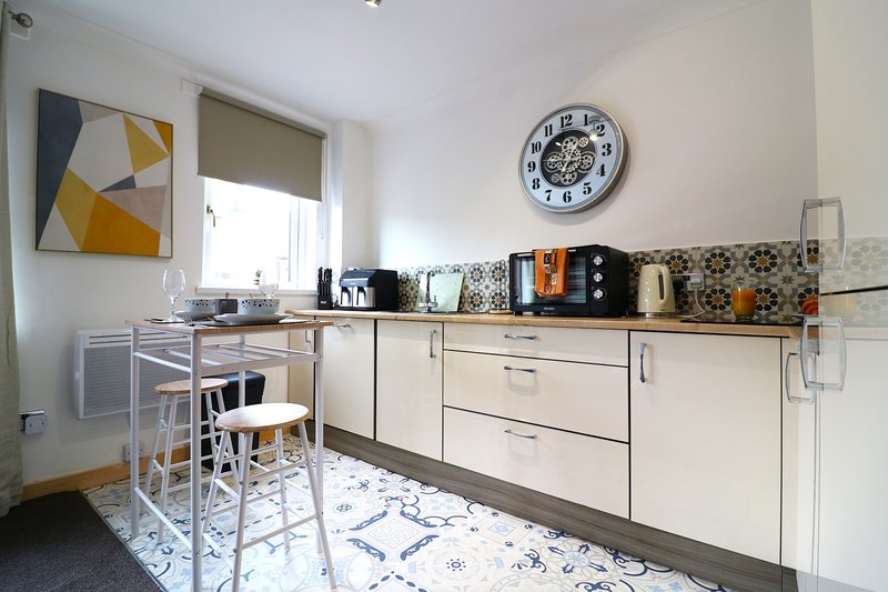 Modern kitchen with white cabinets, geometric backsplash, breakfast bar seating, and wall clock