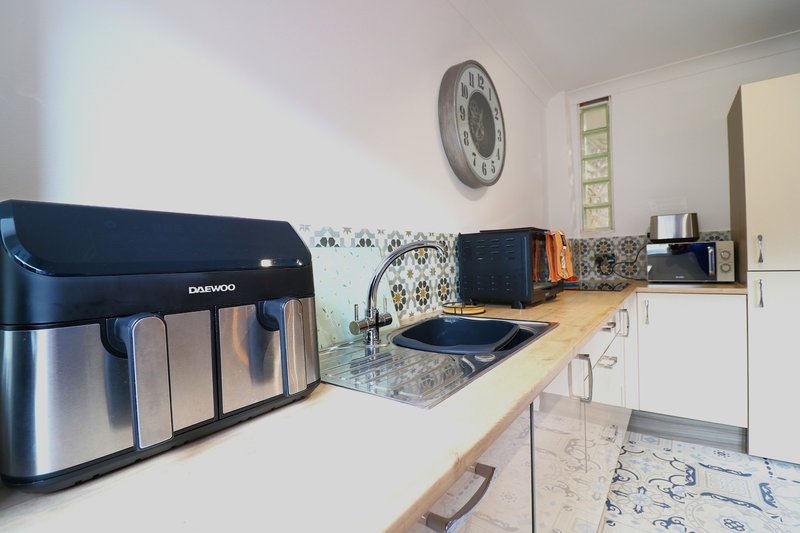 Modern kitchen with wooden countertop, white cabinets, air fryer, and wall clock