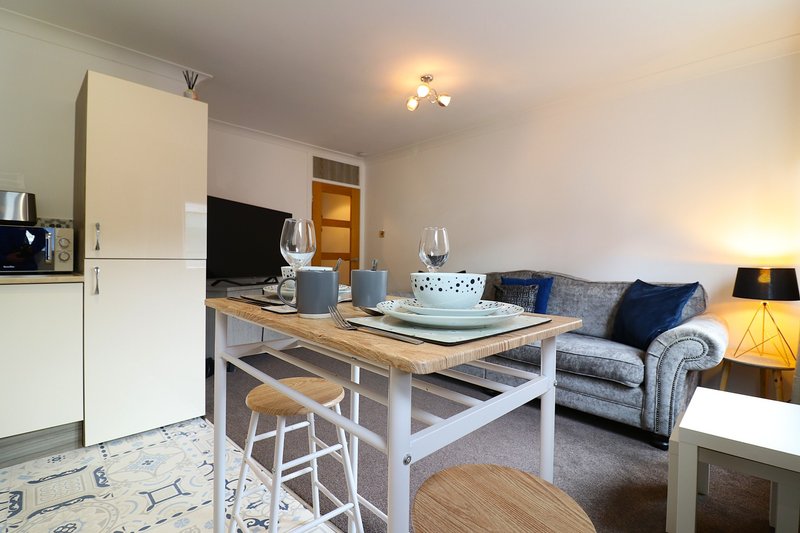 Open-plan living room with dining table, kitchen area, sofa and television
