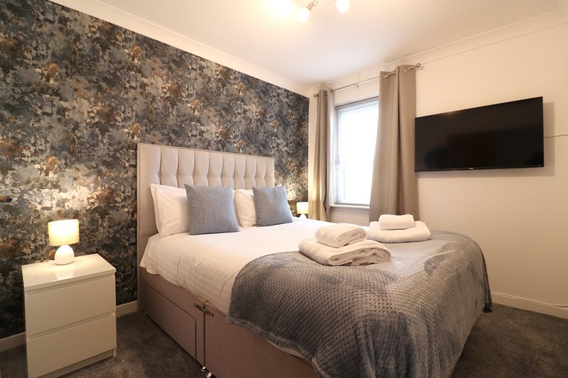 Modern bedroom with double bed, patterned accent wall, wall-mounted TV and bedside lamps