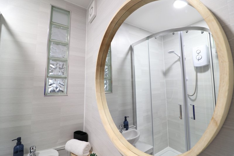 Modern bathroom with round illuminated mirror, walk-in shower enclosure and white subway tiles