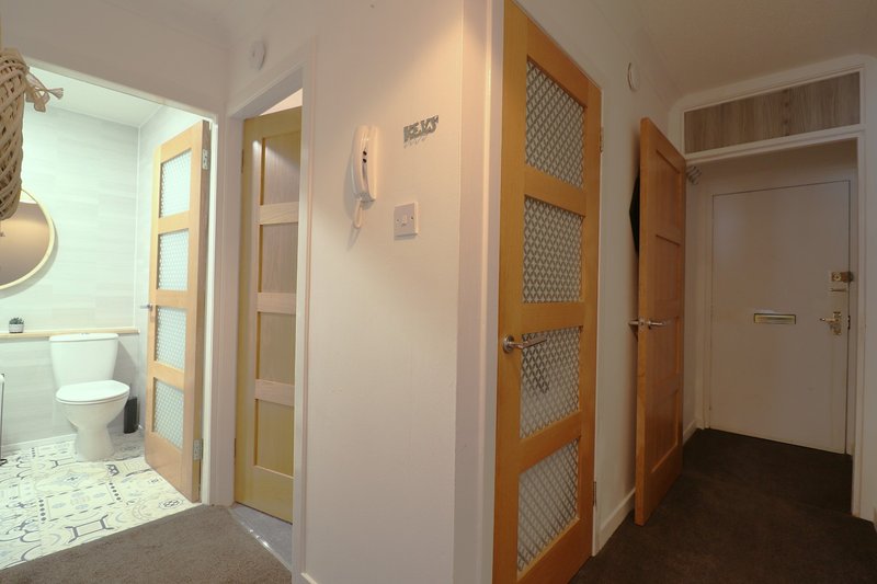 Hallway with bathroom doorway, wooden doors, neutral walls and tiled flooring