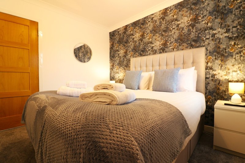 Modern bedroom with double bed, patterned headboard, gold wallpaper accent wall and wooden door