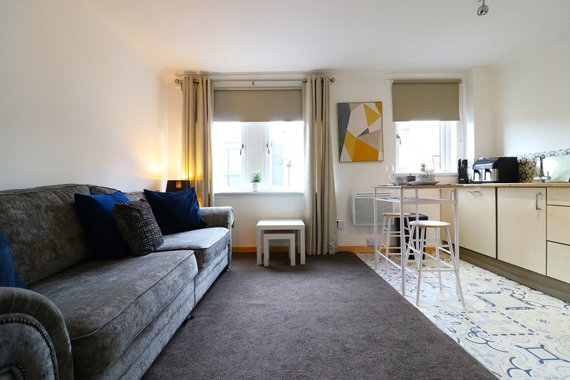 Open-plan living and kitchen area with grey sofa, blue cushions, dining table and neutral décor