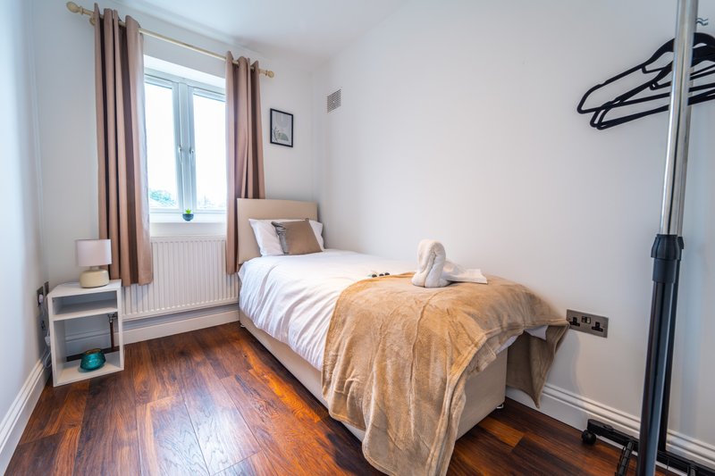 Bedroom with single bed, wooden floor, window with curtains, and radiator