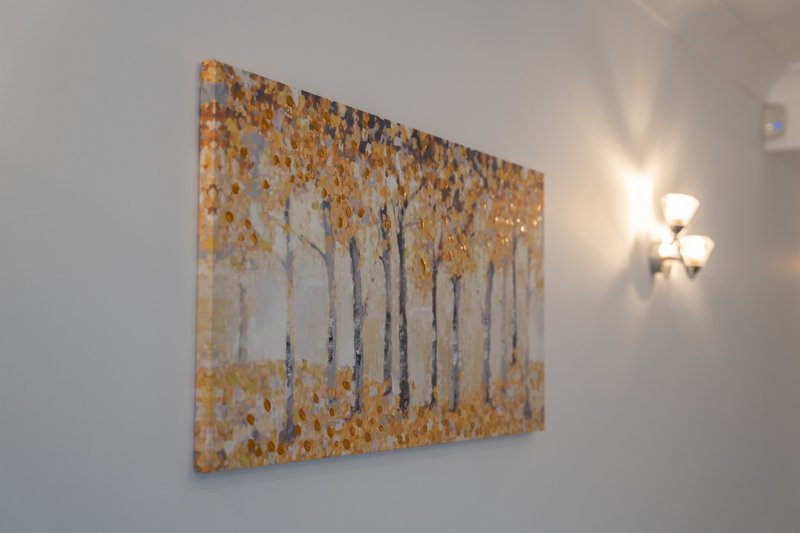 Wall-mounted abstract artwork with golden and grey tones, beside a wall sconce light fixture