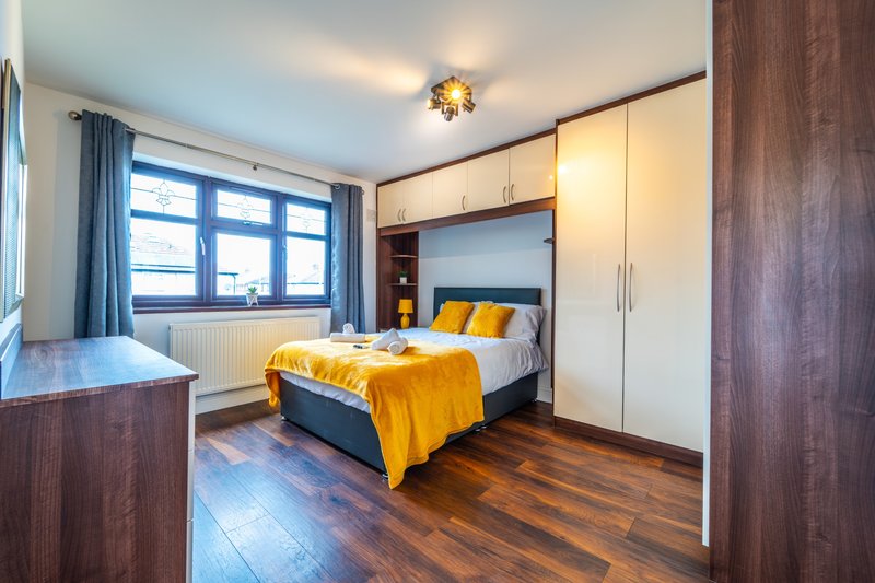 Modern bedroom with double bed, yellow bedding, built-in wardrobes and wooden flooring