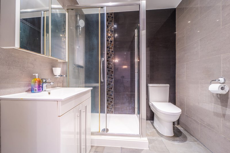 Modern bathroom with white vanity, shower enclosure, toilet, and tiled walls
