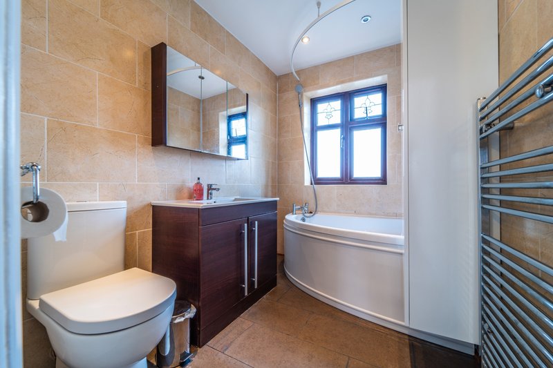 Modern bathroom with toilet, vanity sink, bathtub, heated towel rail and window