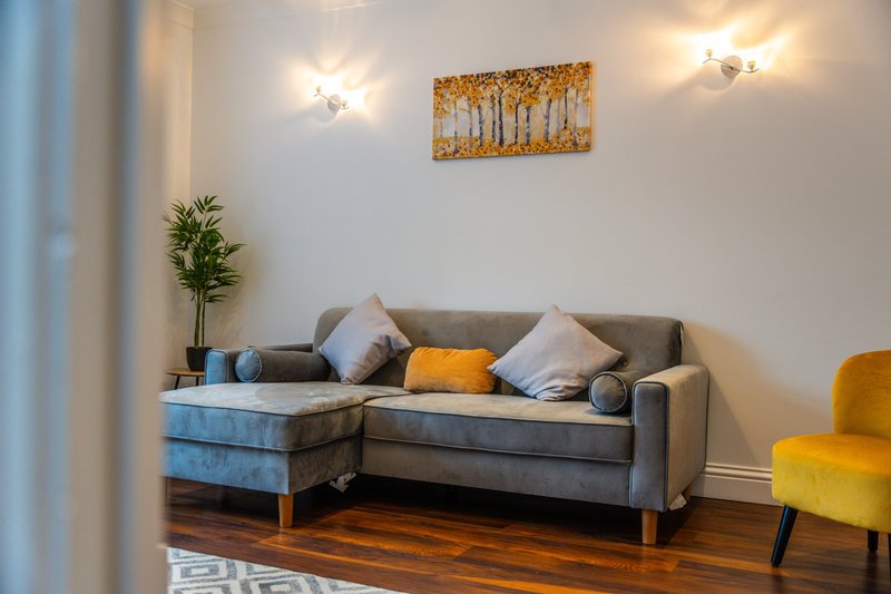 Modern living room with grey sectional sofa, decorative cushions, wall art, and potted plant