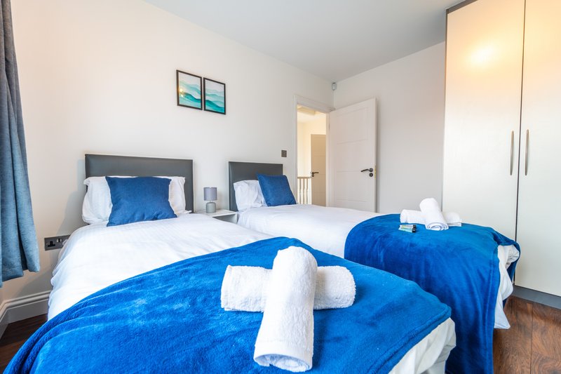 Bright modern bedroom with two beds, blue bedding, white pillows and towels, wardrobe