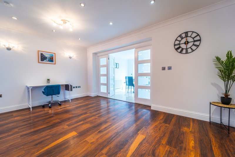 Bright modern living room with wooden floor, glass doors, blue chair and wall clock