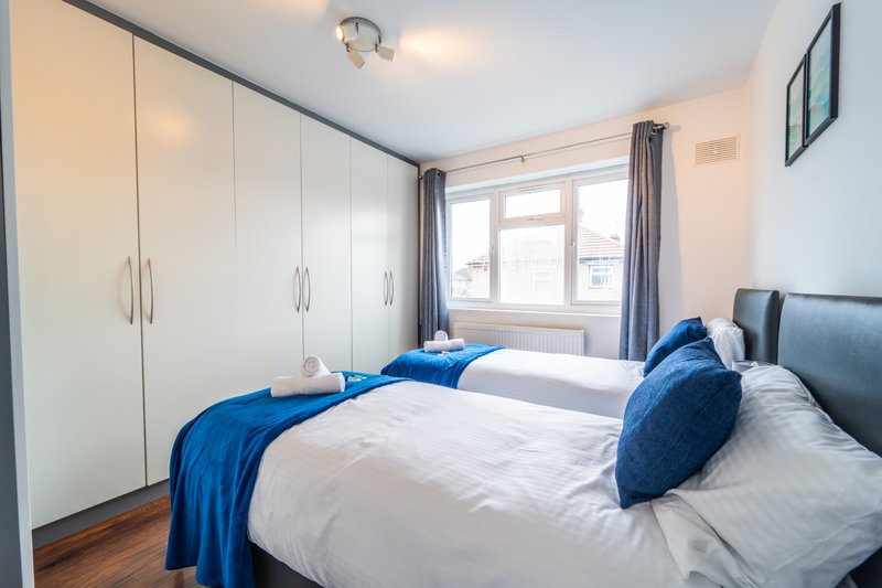 Bright bedroom with two single beds, blue bedding, white wardrobe and window with curtains