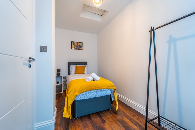Small bedroom with single bed, yellow bedding, wooden floor and wall-mounted clothing rail