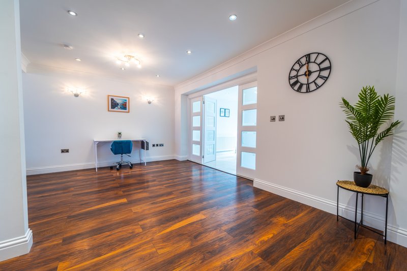 Spacious modern interior with hardwood floors, blue chair, wall clock, and potted plant