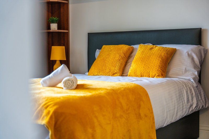 Modern bedroom with double bed, yellow cushions, throw blanket, bedside lamp and wooden shelving