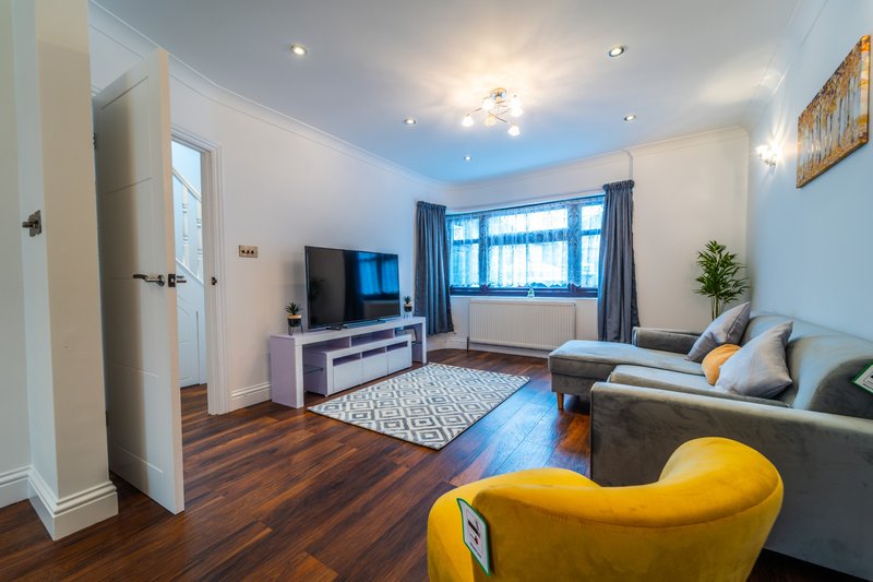 Modern living room with grey sofa, yellow armchair, TV unit, wooden floor and large windows
