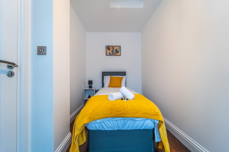 Narrow bedroom with single bed, yellow duvet, white walls and small bedside table