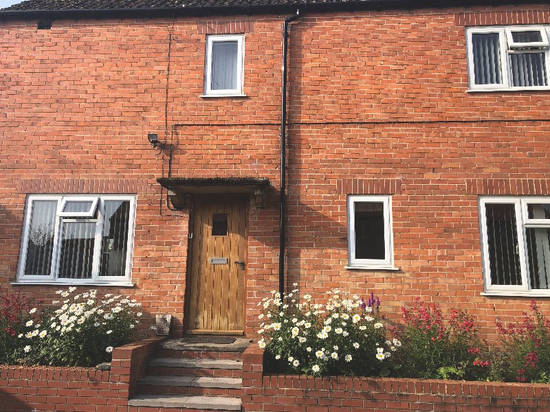 Red brick exterior of residential property with wooden door, windows, and flowering plants