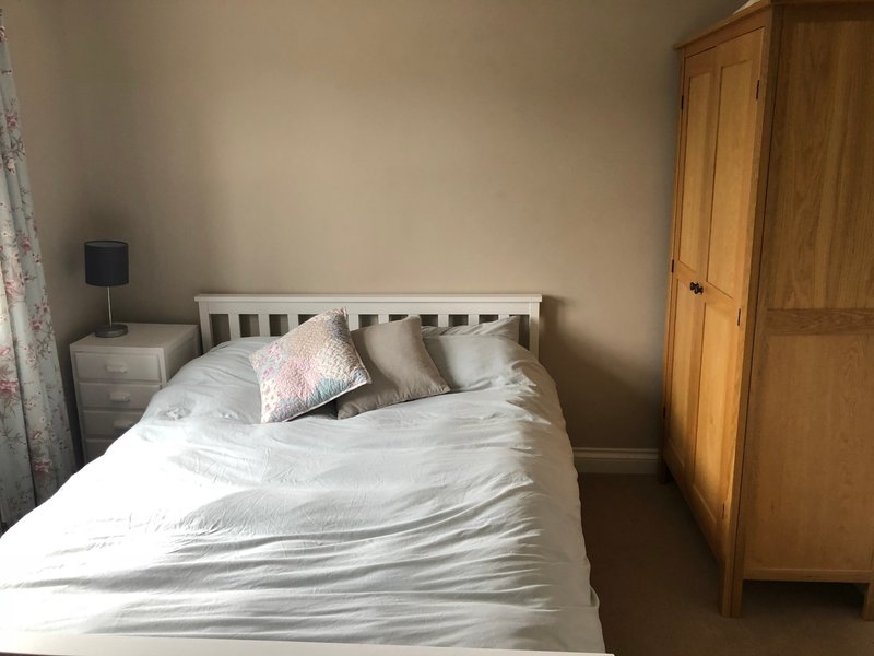 Bedroom with white wooden bed frame, white bedding, decorative pillows, wooden wardrobe and bedside table